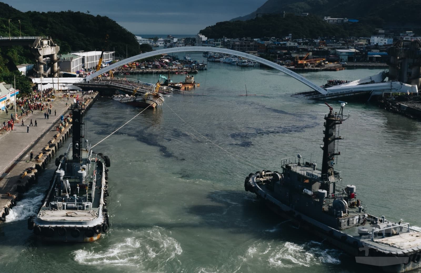 1 October 2019, the day the bridge fell. The navy sent tugs to drag the fishing boats out from under the collapsed deck so that rescuers could get in to search. The quayside is lined with people.
