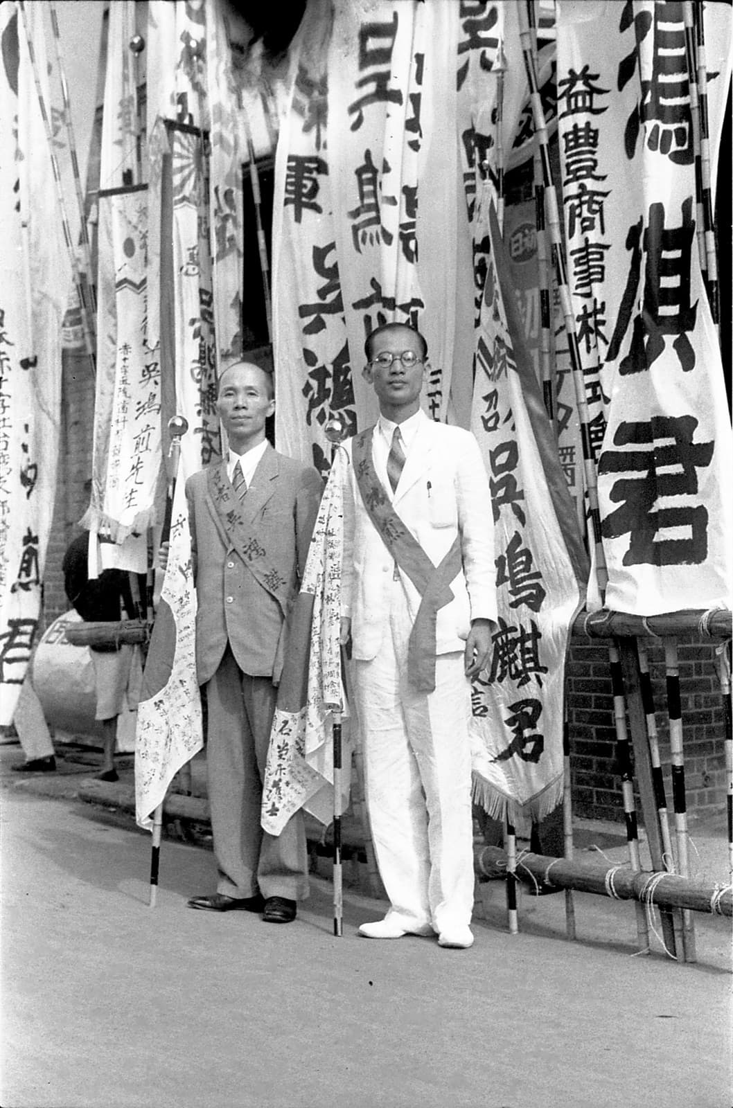 Taoyuan, 1940. Two Taiwanese men about to enlist stand before send-off banners bearing the names of local businesses. This was the army's special volunteer scheme; two years later the Takasago units were sent to the rainforests of the south.